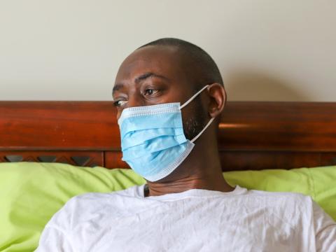 Black man wearing mask in bed