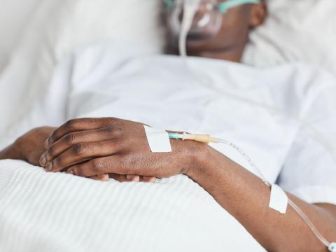 Man in hospital bed with oxygen mask, IV port