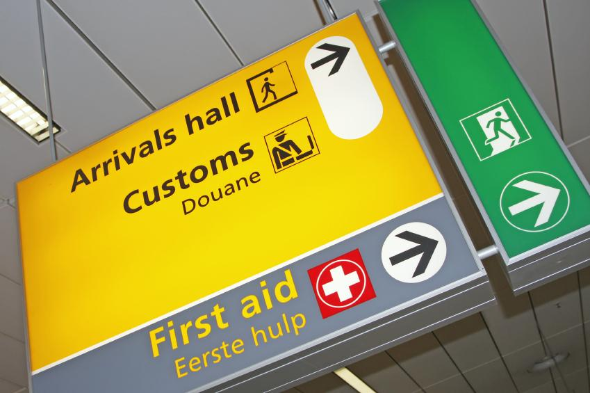 Sign at airport with arrows to arrival hall, customs, and first aid