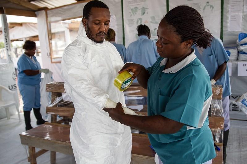 Nurse helping aid worker don personal protective equipment