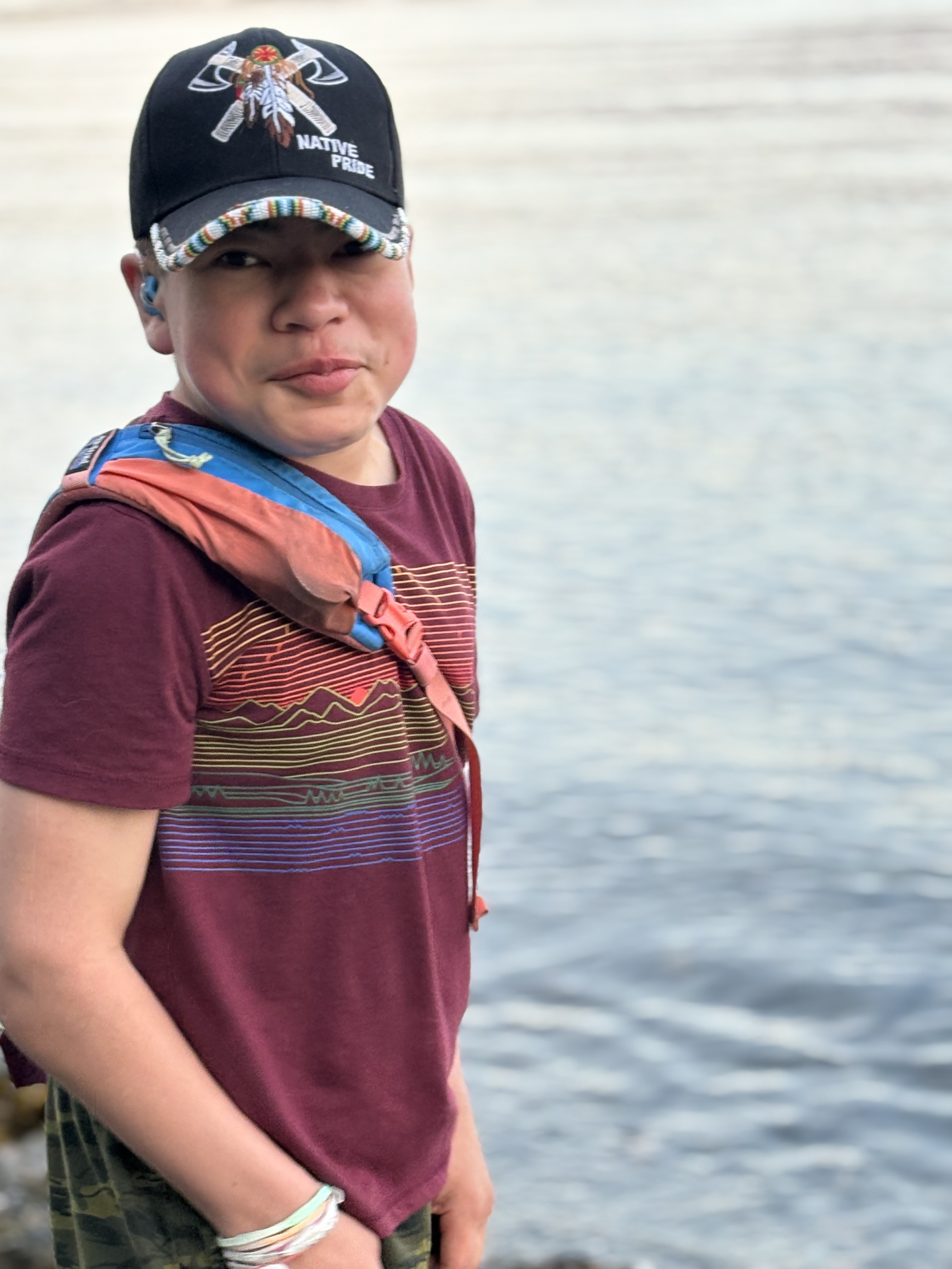 Native American boy wearing a black Native Pride hat and smiling