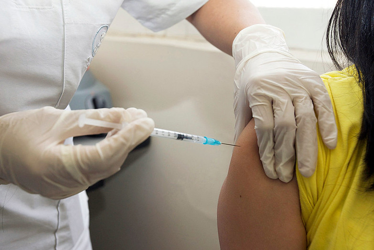 A close-up of a nurse vaccinating a teen girl.