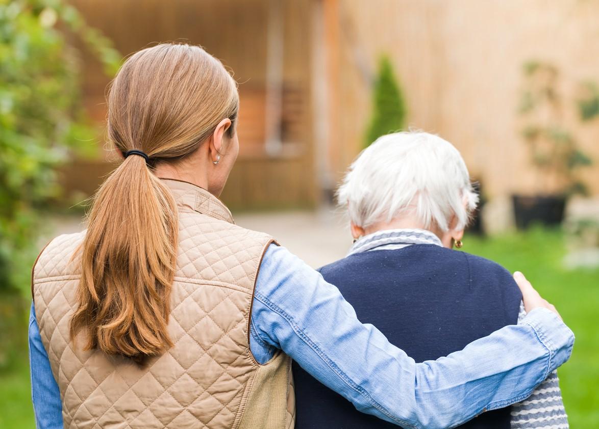 Caregiver helping older woman walk outside