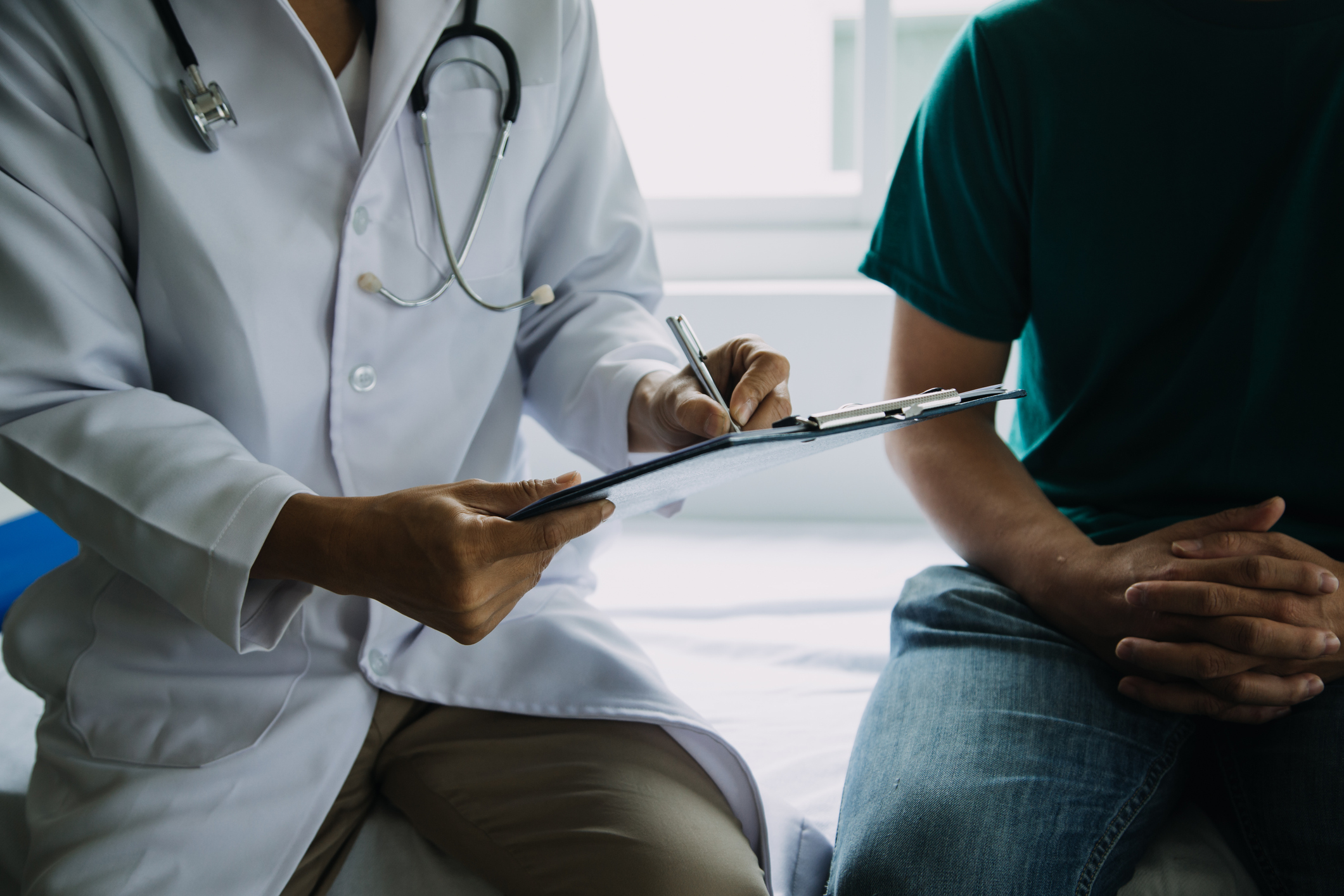 Doctor in white lab coat with chart sitting next to male patient