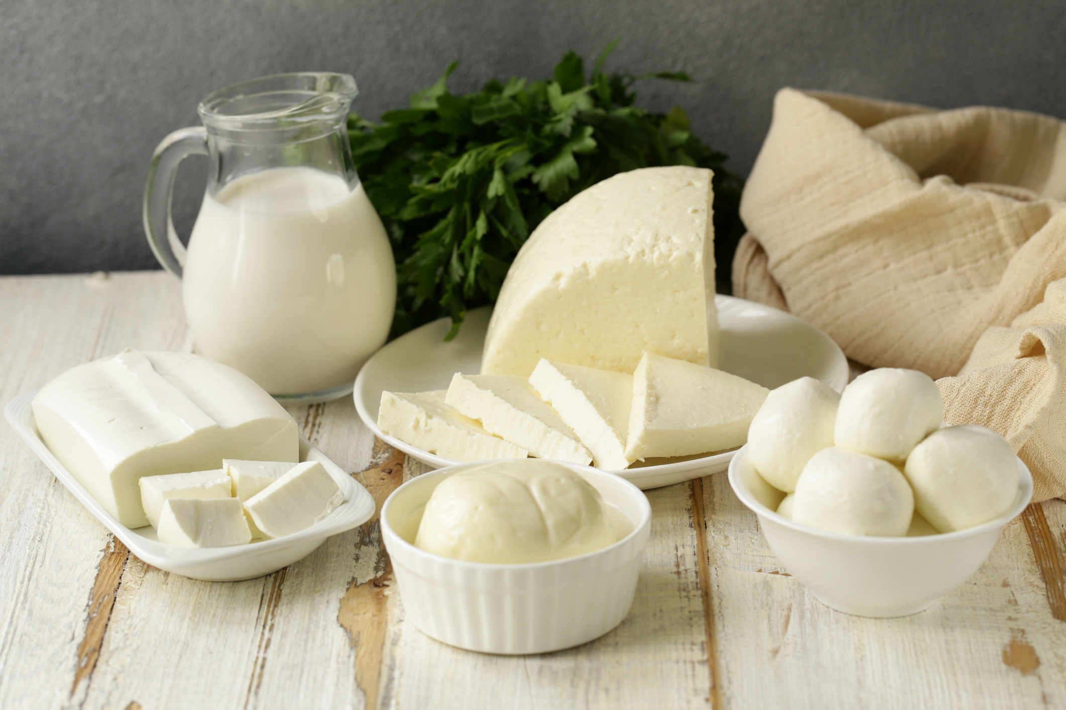A rustic wooden table set with milk and various white cheeses.