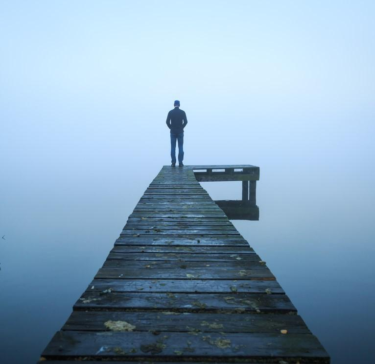 Person standing at end of dock in fog