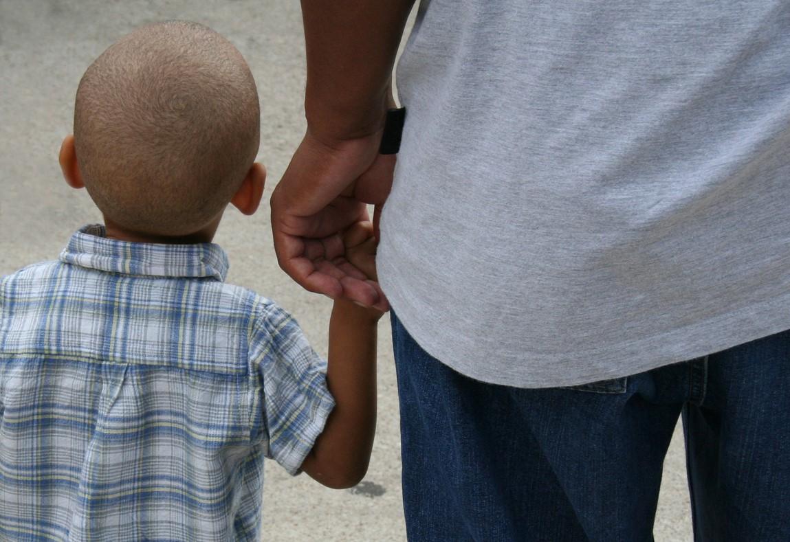Back view of little boy holding his dad's hand