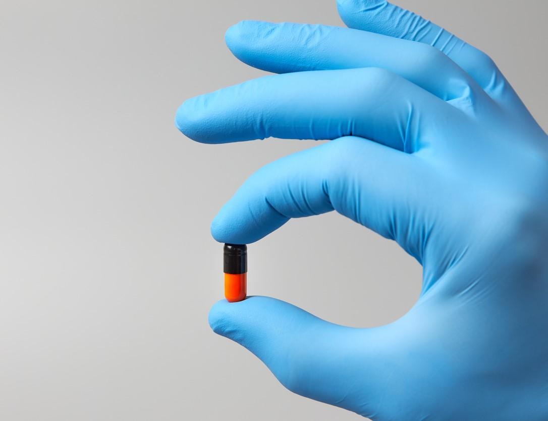 Black and orange capsule in gloved hand