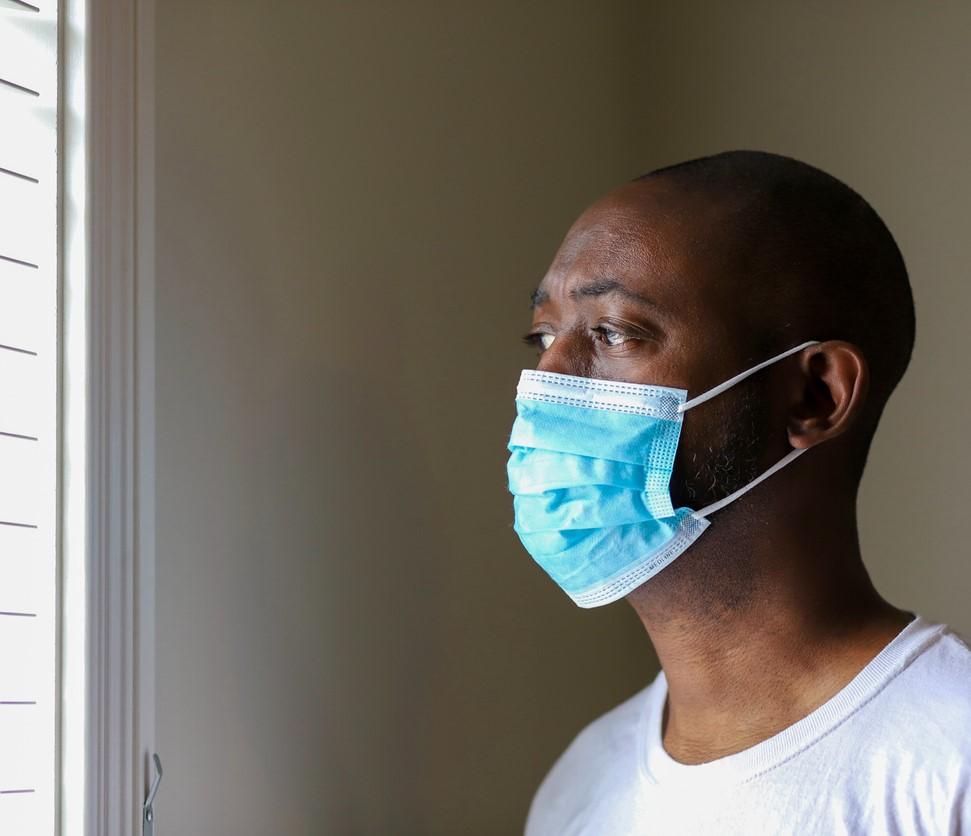 Black man wearing mask looks out window