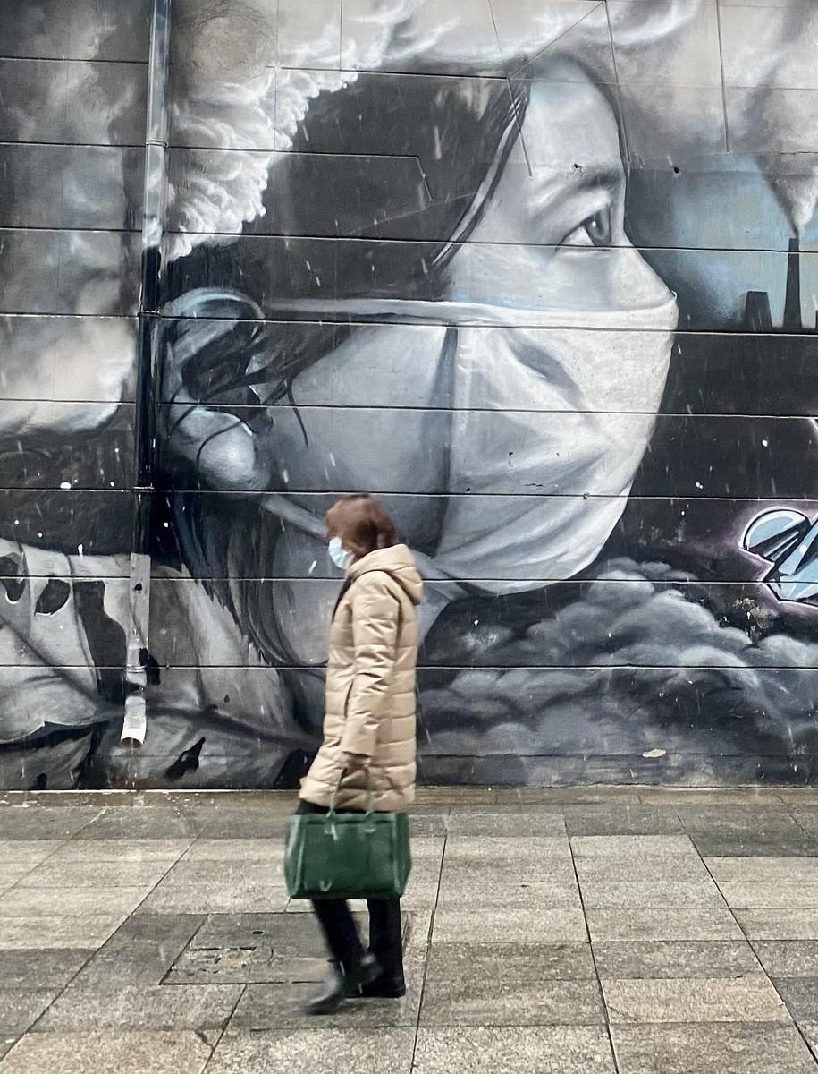 Chinese woman with mask in front of mask mural