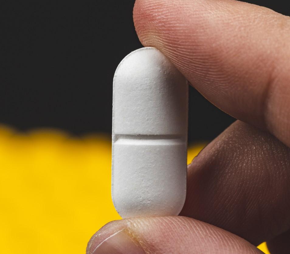 Closeup of fingers holding a white pill
