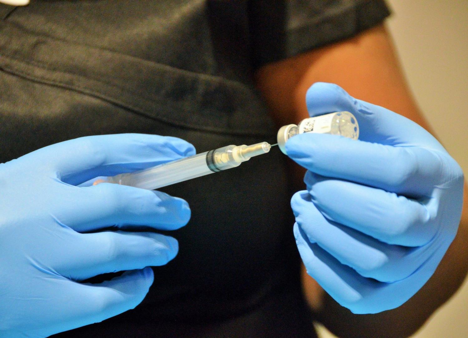Gloved hands drawing COVID vaccine into syringe