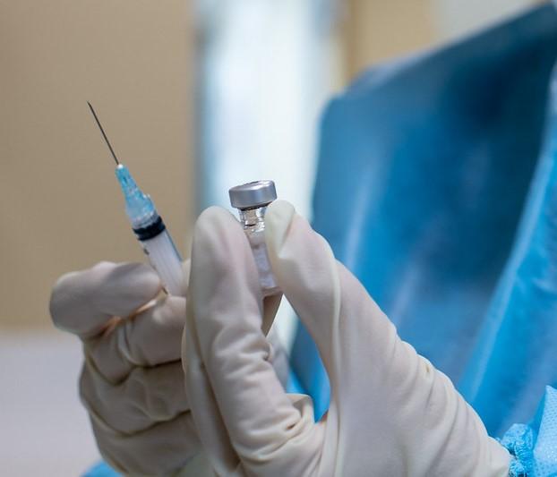 Gloved hands holding COVID vaccine vial and syringe
