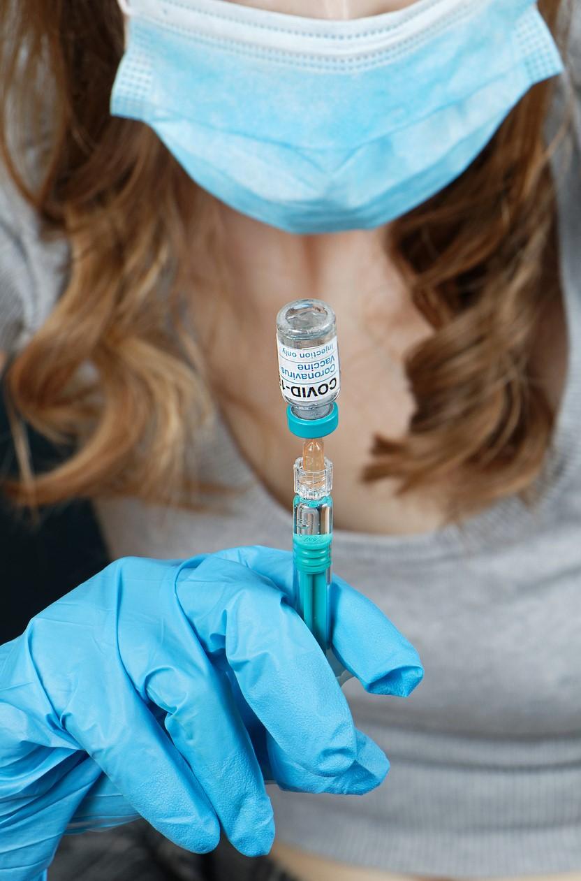 Health worker holding COVID vaccine vial upside down with syringe