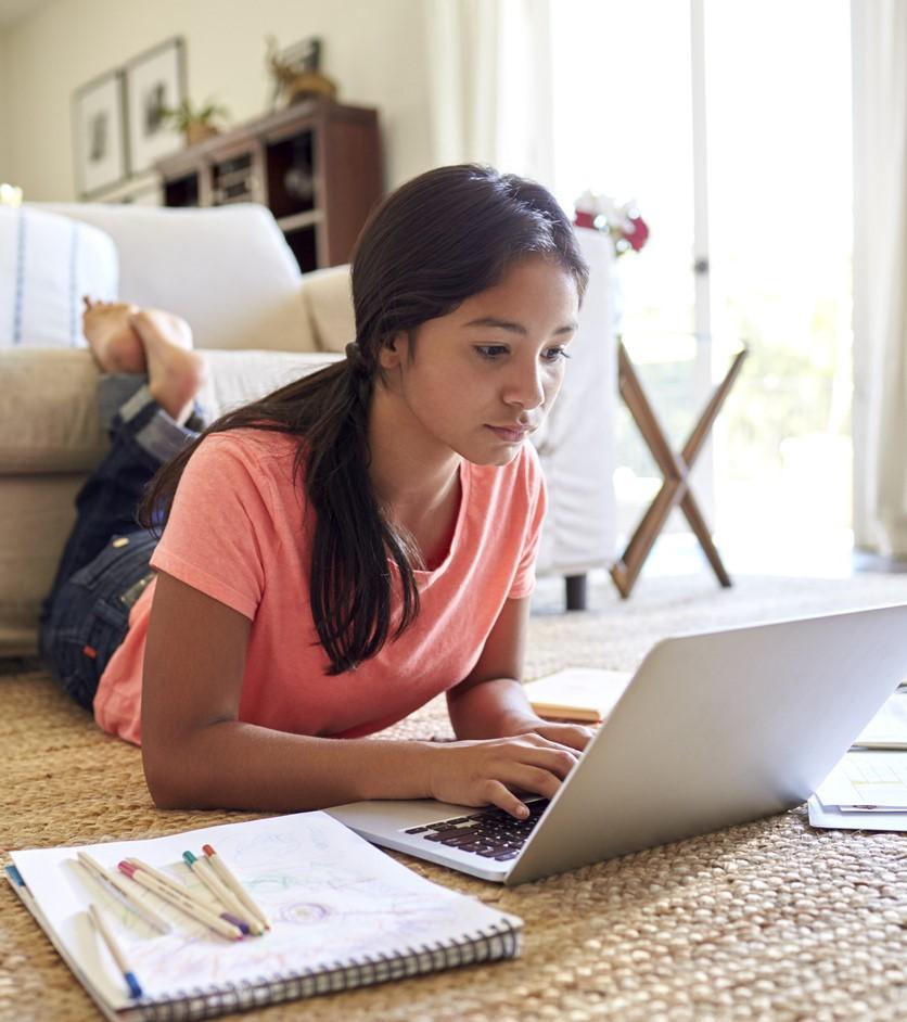 Teen on floor doing homework on laptop
