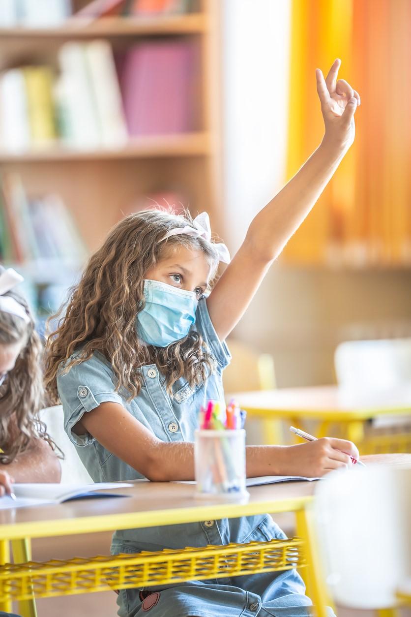 Mask-wearing girl in school raising hand