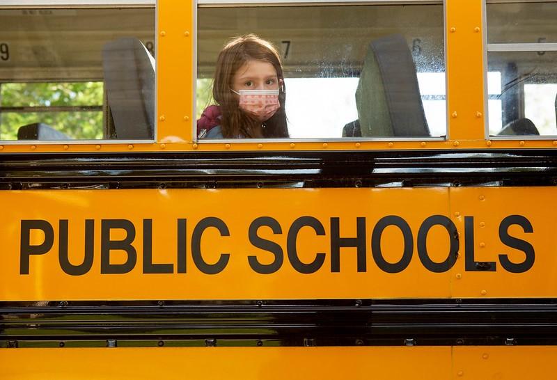 Masked schoolgirl looks out bus window
