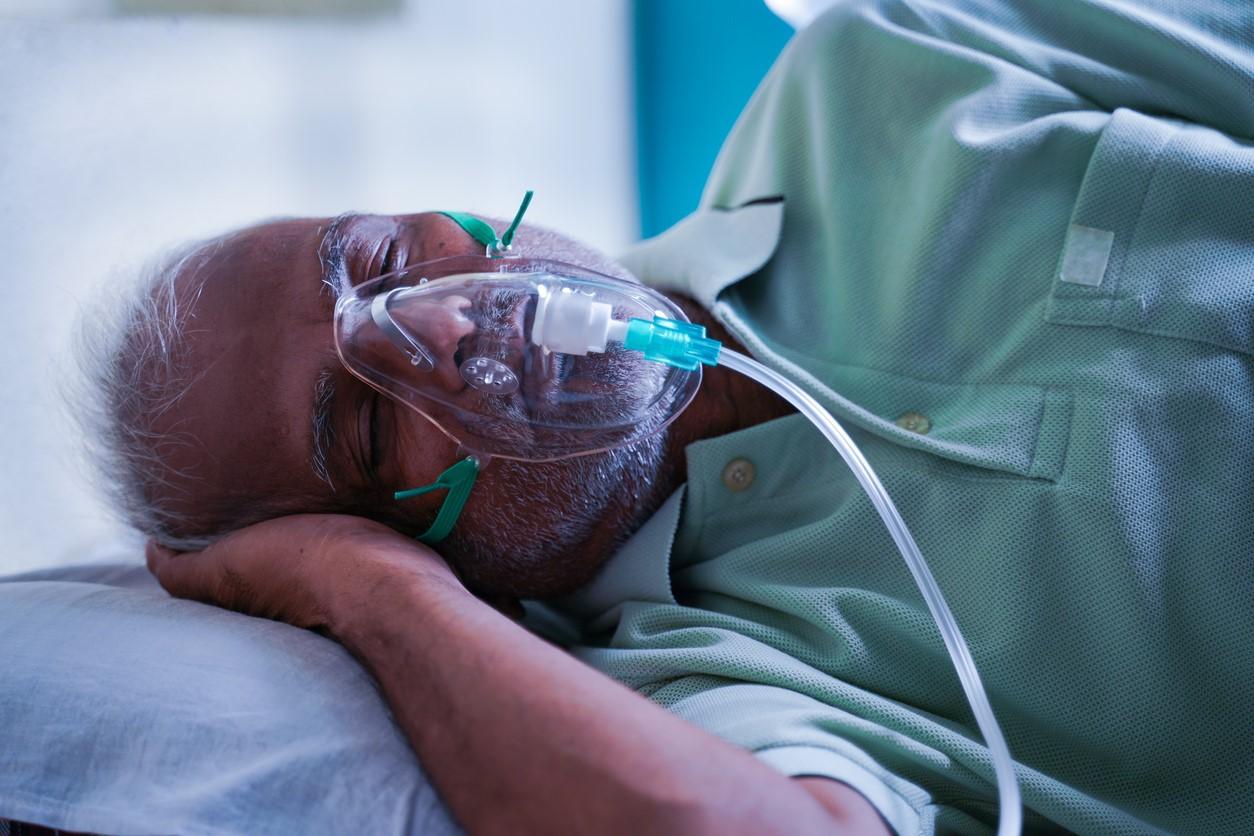 Older man wearing oxygen mask, lying on his side