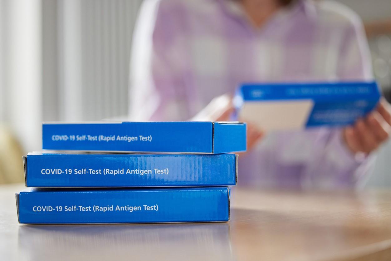 Stack of rapid COVID tests, woman in background