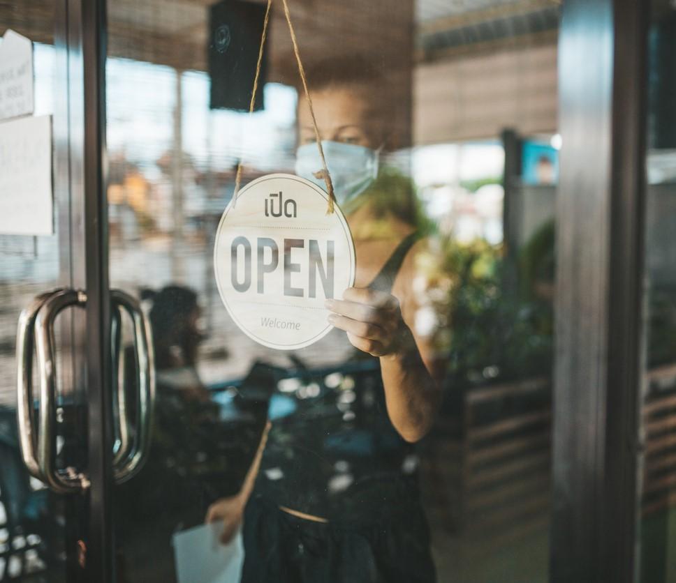 Store owner with mask and "open" sign