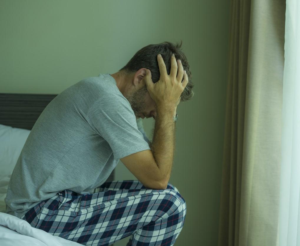 Stressed man sitting on edge of bed