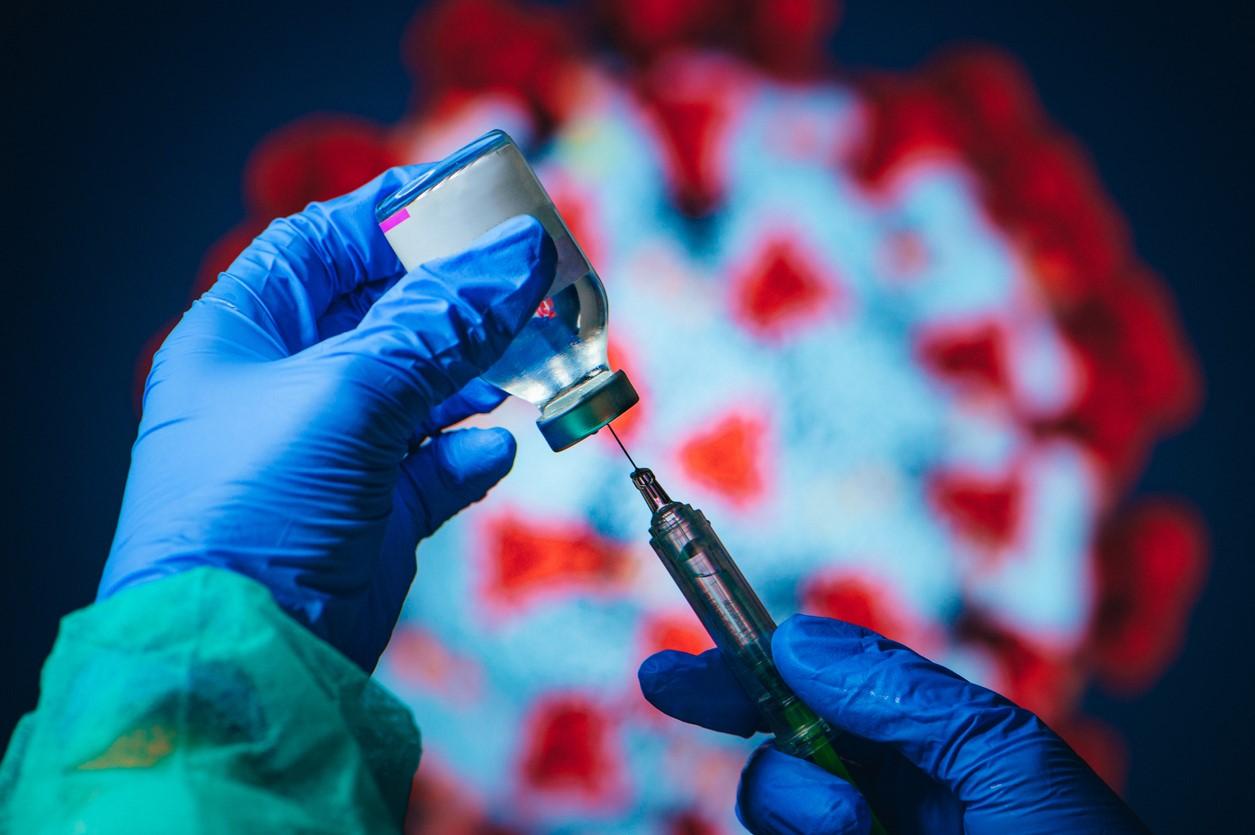 Vaccine vial and syringe in front of a virus image