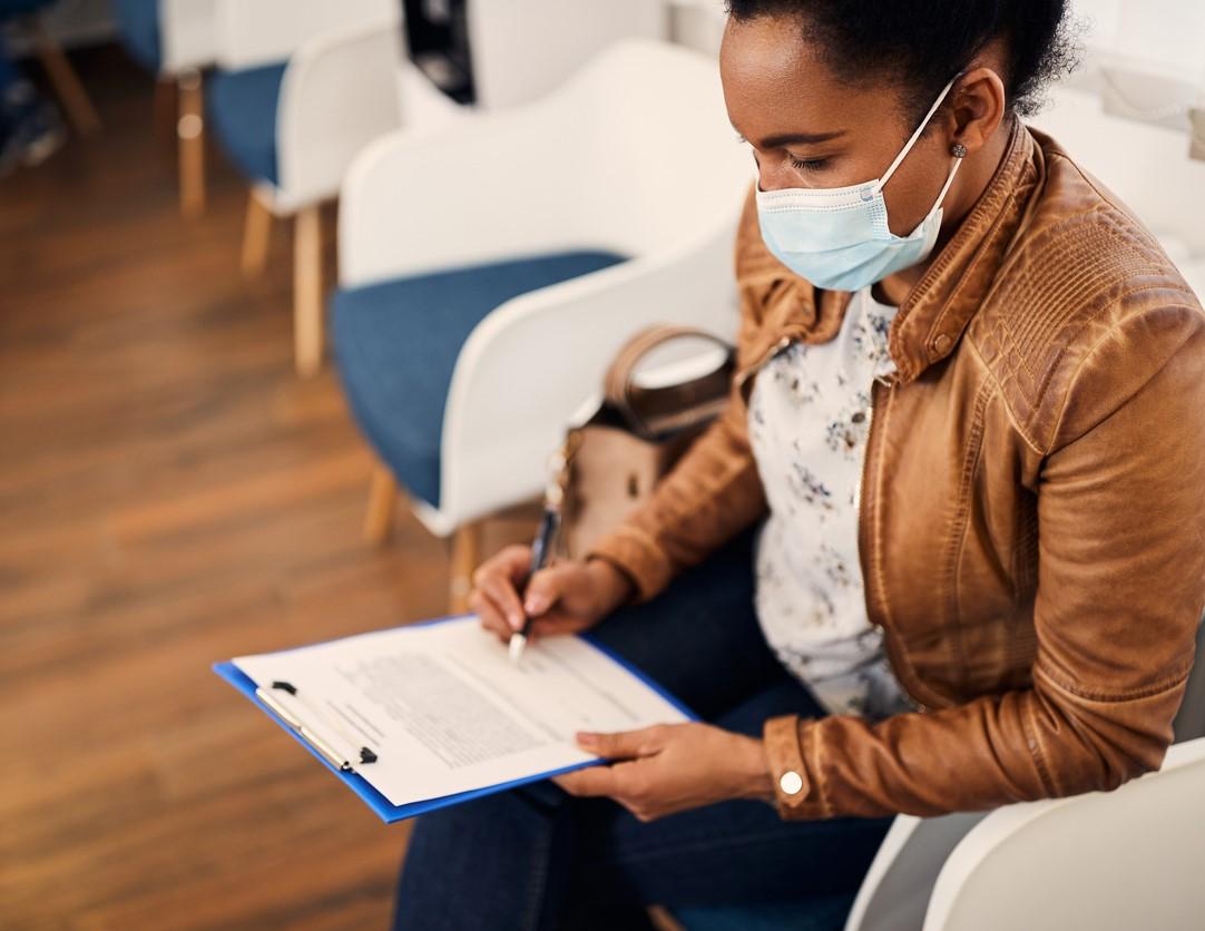 Woman in medical mask filling out healthcare paperwork
