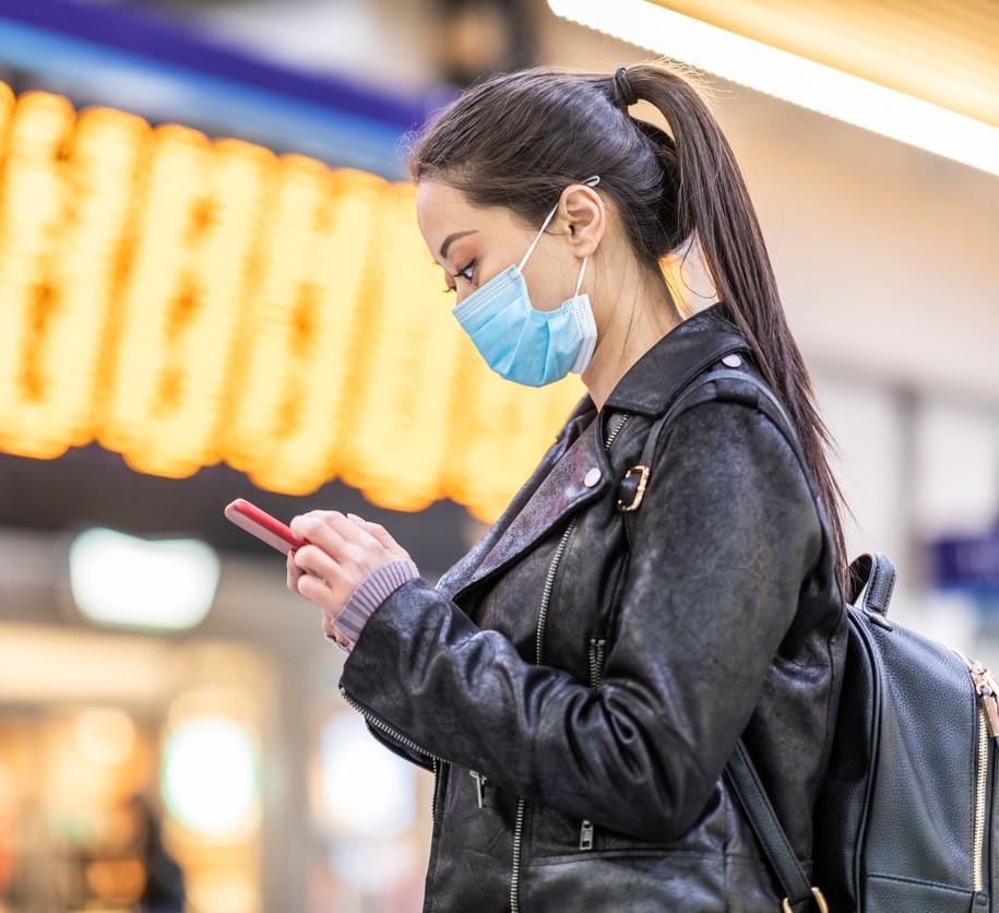 Woman with mask and cell phone at train station