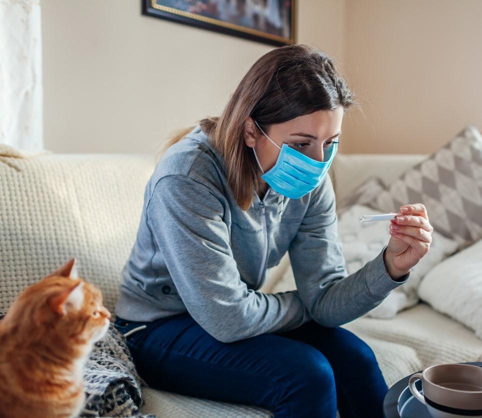 Woman wearing mask at home checking her temperature