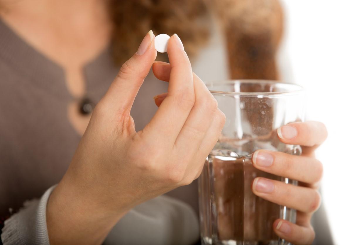 Woman holding white pill and glass of water