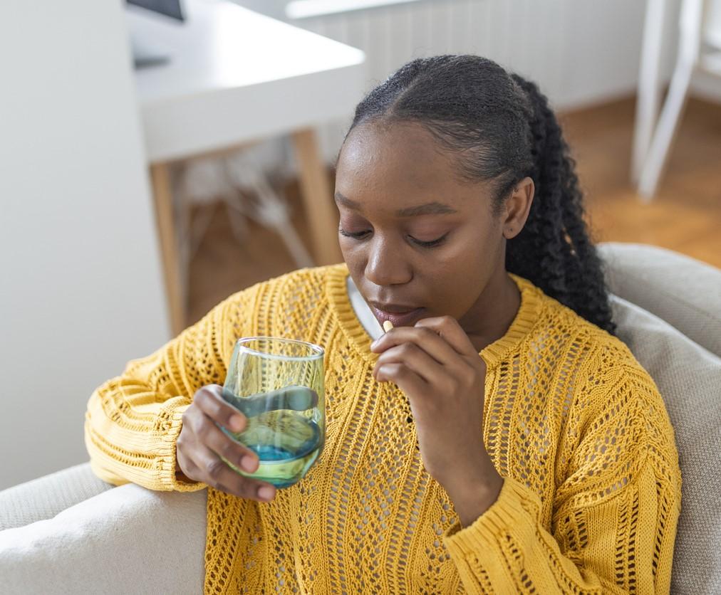 Young woman on couch taking pill