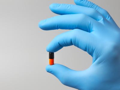 Black and orange capsule in gloved hand