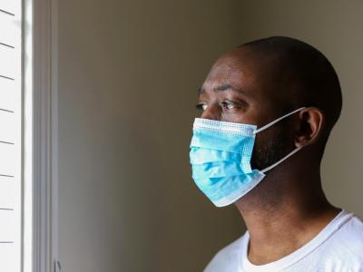 Black man wearing mask looks out window
