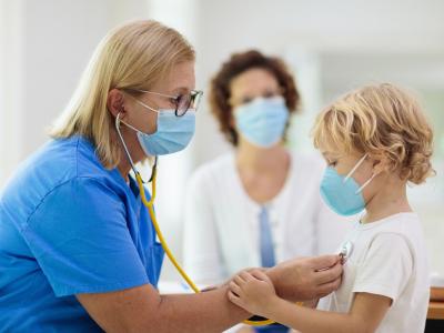 Doc with stethoscope examining child wearing a mask