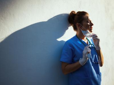 Exhausted health worker taking off mask, leaning on wall