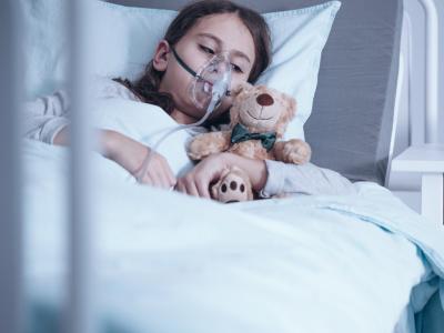 Girl on oxygen holding teddy bear in hospital bed