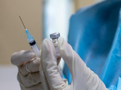Gloved hands holding COVID vaccine vial and syringe