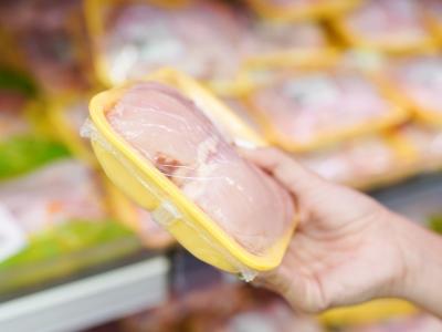 Hand holding packaged chicken in grocery store