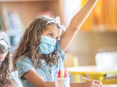 Mask-wearing girl in school raising hand