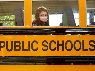 Masked schoolgirl looks out bus window