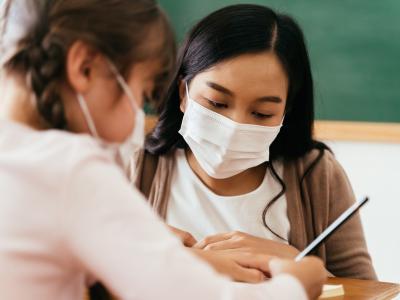 Masked teacher helping masked student