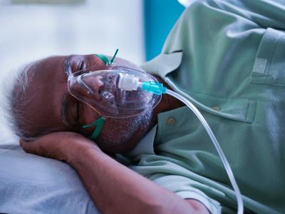 Older man wearing oxygen mask, lying on his side