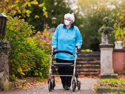 Older woman wearing mask outside using walker