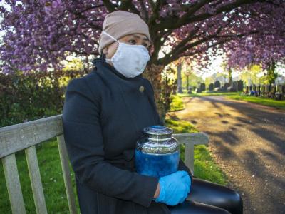 Woman wearing mask and holding urn in cemetary