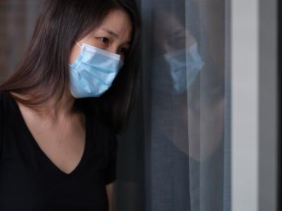 Sad woman wearing mask and her reflection in window