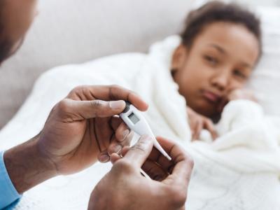 Sick girl in bed with dad taking her temperature