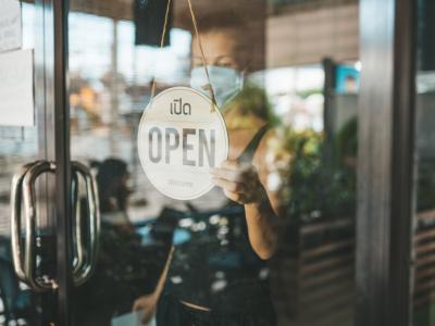 Store owner with mask and "open" sign