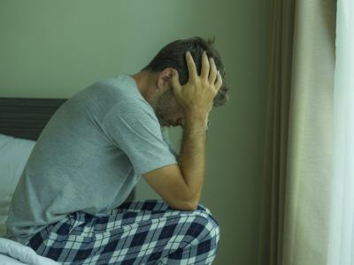 Stressed man sitting on edge of bed