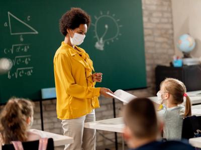 Masked teacher handing out a test