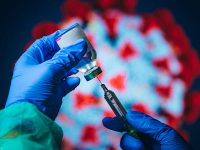 Vaccine vial and syringe in front of a virus image